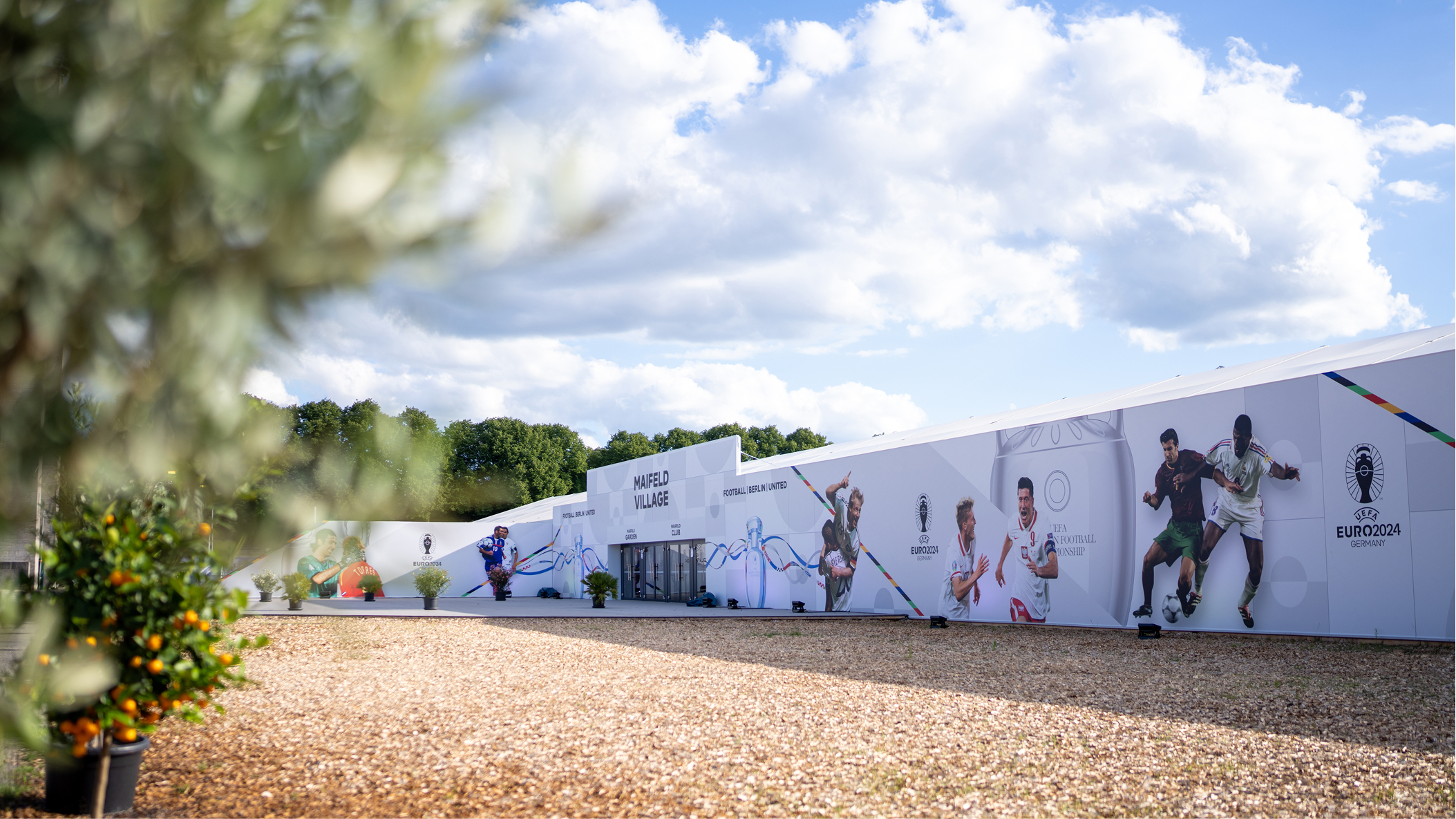 Außenansicht des UEFA EURO 2024 Maifeld Village mit Textilhülle und bepflanztem Vorbereich