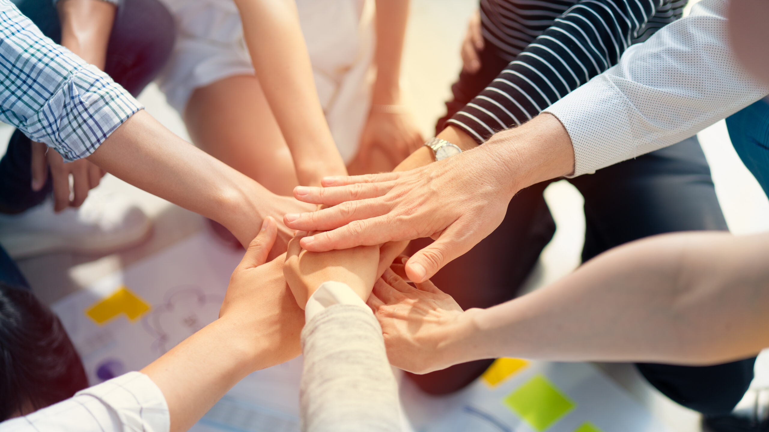 Mehrere Hände verschiedener Personen übereinander als Zeichen von Teamwork
